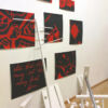 Installation mit rotschwarzen Acrylbildern und weiß bemalten Holzstangen